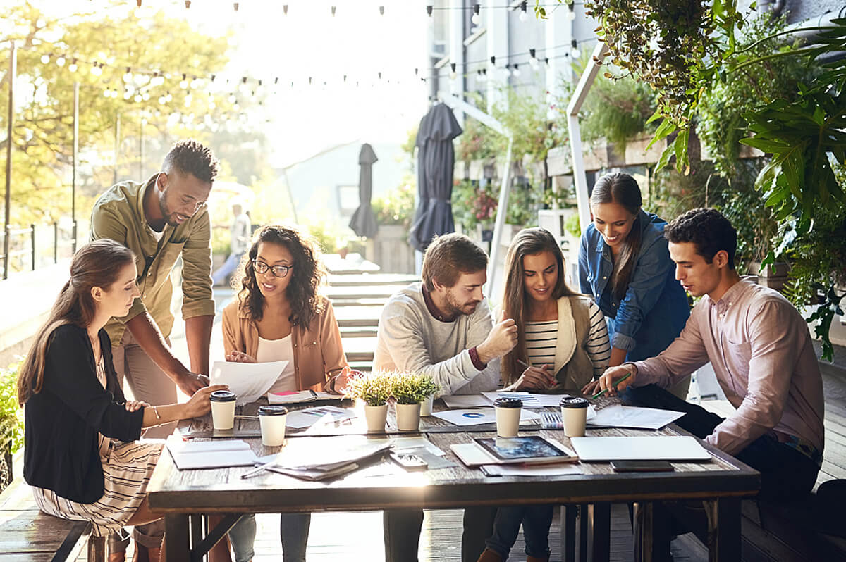 A team of young adults sitting outside and working at a table with papers scattered