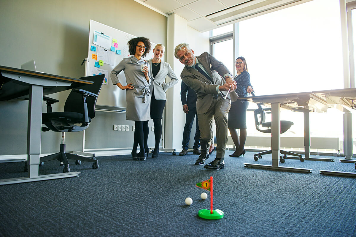 Multiple business professionals playing mini-golf game in communal office setting